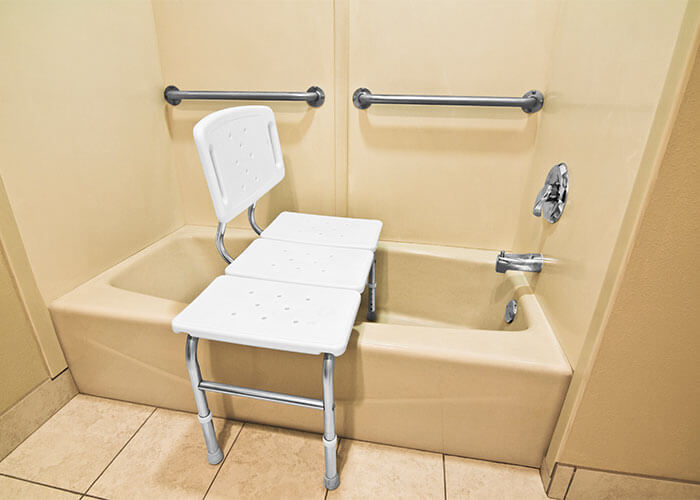 Photo featuring a bathtub with grab bars above it and a bath bench in it.