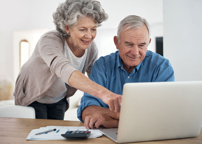 Older couple pointing and looking at screen on laptop together.